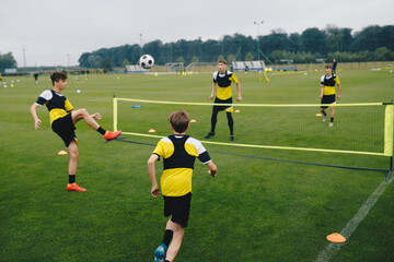 Wall Mural - Young boys in youth soccer club playing football tennis training game. Teenage soccer players playing football tennis on training session. Teenagers practicing soccer on grass pitch.