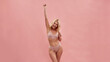 © Svitlana - Happiness. Excited beautiful middle aged caucasian blonde woman wearing underwear dancing and having fun while posing isolated over pink background