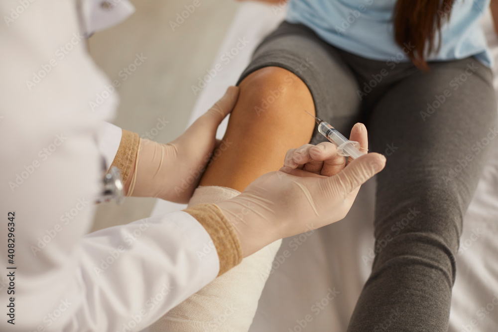Close up of a doctor giving an injection in the knee to a patient who has an injured leg. Female patient treats leg injury in modern medical clinic. Concept of treating foot problems. - obrazy, fototapety, plakaty 