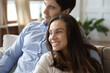 © fizkes - Close up dreamy smiling couple hugging, visualizing good future, looking to aside, sitting on cozy couch at home, happy man and woman cuddling, dreaming together, planning, enjoying lazy weekend