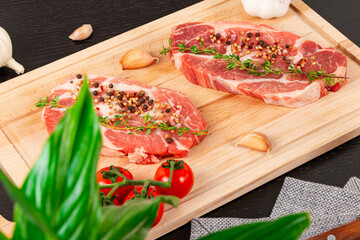 freshly chopped raw pork steaks with spices and thyme on a cutting board. next to ripe red tomatoes and garlic