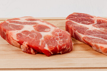 fresh raw marbled pork steak on a solid beech wood cutting board on a white table