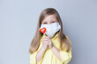 valentine's day caucasian child holding a lollipop heart over grey background. Face mask.Donation,heart health,world heart day, world health day,world mental health day.Health and heart concept.