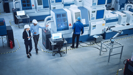 Fototapete - Industry Four Factory: Female Executive and Chief Engineer Inspect Facility Workshop, Look at robot arm working on Assembly Line. High-End CNC Machinery and Equipment. High Angle