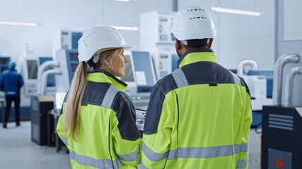 Industry 4.0 Factory: Chief Engineer and Project Supervisor in Safety Vests and Hard Hats, Talk, Use Digital Tablet Computer, Screen Shows 3D Concept of New Engine. Industrial Workshop with Machinery