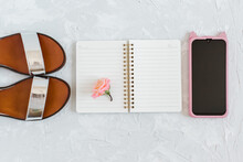Flat Lay Composition With Stylish Woman's Accessories On Light Grey Background. Notebook, Sandals, Flower, Mobile Phone.