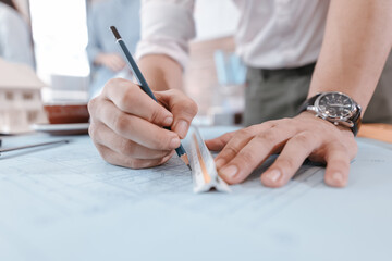 engineers holding a pen pointing to a building and  drawing outlay construction plan as guide for builders with details. Engineer design and writing blueprint.