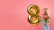 Carefree young lady with golden number eight balloon and bunch of tulips posing on pink background, copy space