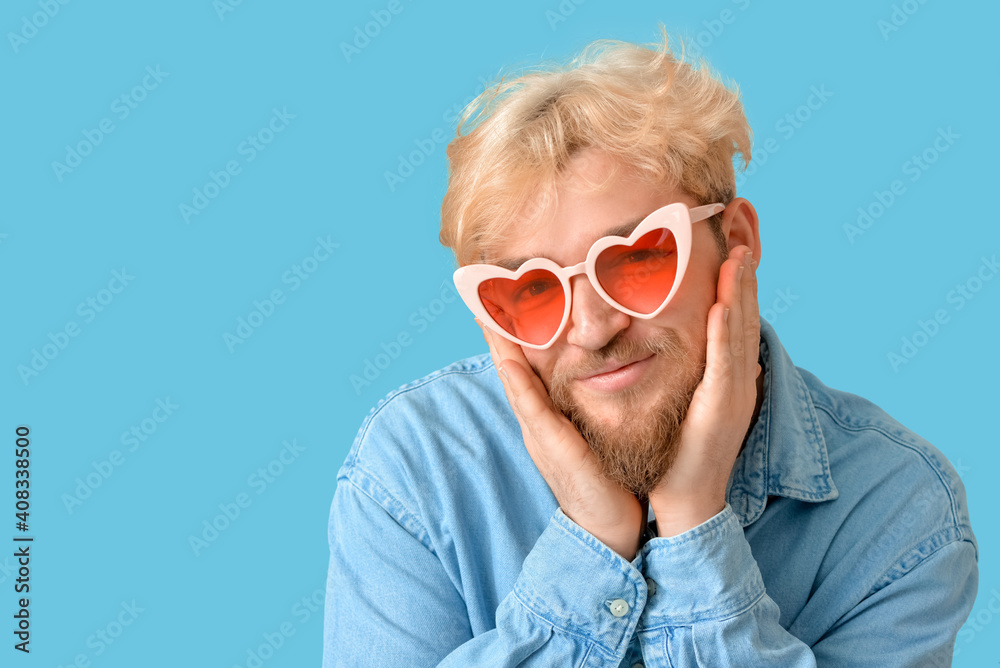 Cute man wearing heart-shaped glasses on color background
