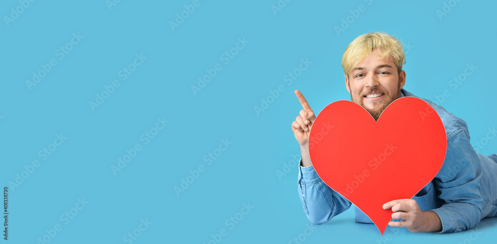 Handsome man with big red heart pointing at something on color background