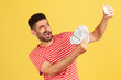 © khosrork - Extremely happy satisfied man blogger in striped t-shirt making selfie photo with bunch of dollar banknotes on smartphone and winking, bragging with wealth