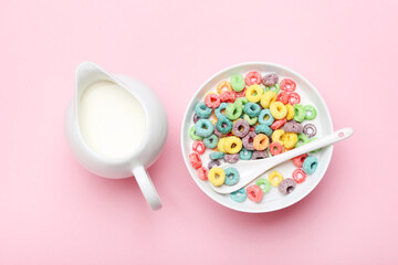 Colorful corn rings in bowl with milk and spoon on pink background