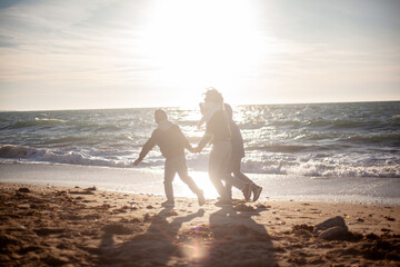 Happy family, mother with sons walking wirh fun in the sea shore on windy day. People dressed warm clothes.