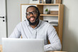 © Vadim Pastuh - Friendly and handsome African-American wearing glasses and headset in the office, sitting at the desk with an open laptop, working in the customer service department as a call center operator