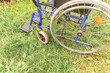 Empty wheelchair standing on grass in hospital park waiting for patient services. Invalid chair for disabled people parked outdoor in nature. Handicap accessible symbol. Health care medical concept.