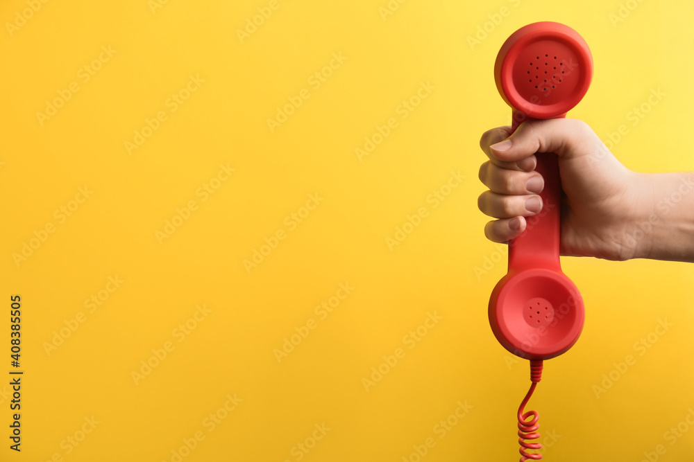Closeup view of woman holding red corded telephone handset on yellow background, space for text. Hotline concept - obrazy, fototapety, plakaty 