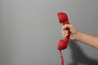 © New Africa - Closeup view of woman holding red corded telephone handset on light grey background, space for text. Hotline concept