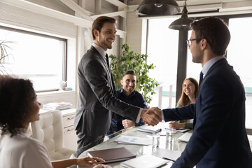 happy business partners shaking hands at corporate meeting, standing in boardroom, making successful