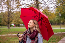 Thoughtful Woman Looking Up With Umbrella In Autumnal Park