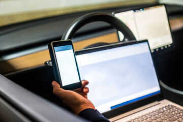 Professional technician with mobile phone and laptop for programming in electric car