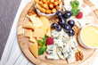 Board with different types of cheese. Cheeses mix set dor blu chedar parmesan brie honey sauce finger bread and grape on wooren palte. Restaurant menu breakfast plate. Healthy snack assortment.