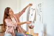 © Veam/Westend61 - Female artist pasting charcoal drawing on wall in living room