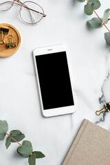 Wall Mural - Home office workspace with smartphone mockup, feminine glasses, notebook, eucalyptus leaves. Flat lay, top view, copy space.