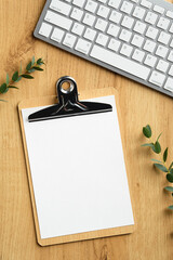 Wall Mural - Wooden office desk table with blank paper clipboard mockup, keyboard, eucalyptus leaves. Top view with copy space, flat lay.
