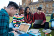 © Jonah Ritchie/Austockphoto - Group of young university students hanging out sitting on grass studying and using devices