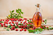 Rosehip oil in glass bottle on wooden table horizontal. Red fluid from berries in clear jar with plants around. Herbal alternative medicine on palette.