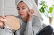 Woman with towel on head applying patches under eyes enriched with collagen, vitamin E, diminishes the signs of aging, helps reduse eye puffiness, looking in mirror. Face skin care beauty at home. 