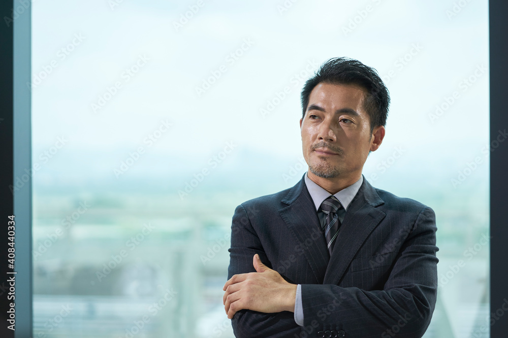 contemplative asian business man standing by windwo in office - obrazy, fototapety, plakaty 