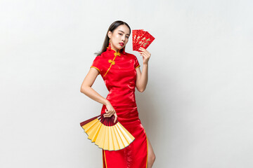 Wall Mural - Asian woman in oriental cheongsam costume holding red envelopes or Ang Pao and fan on light gray studio background for Chinese new year concepts, text means great luck great profit