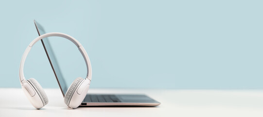 Side view of slim laptop with wireless headphones on grey desk. Blue background. Distant learning. working from home, online courses or support. Audio podcast. Helpdesk or call center headset