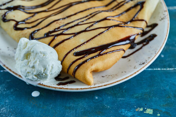 Pancakes with vanilla ice-cream, chocolate on the white plate in the blue background