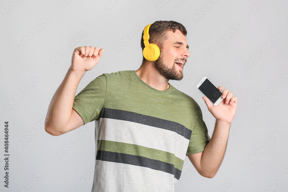 Young man with mobile phone and headphones on light background