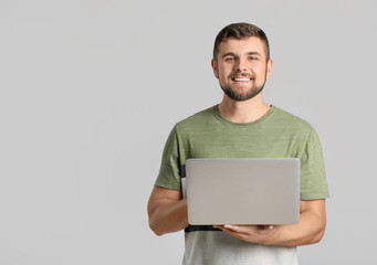 Wall Mural - Young man with laptop on light background