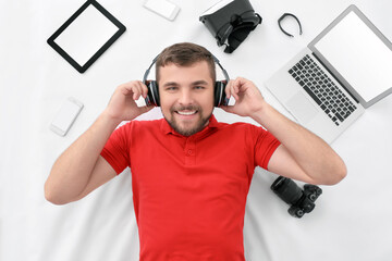 Canvas Print - Young man with different gadgets in headphones on white background