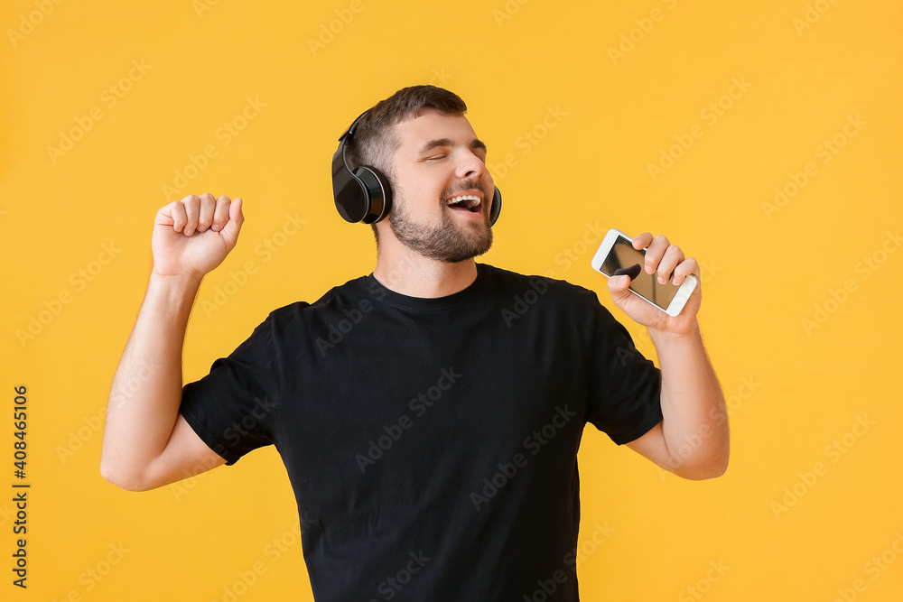 Young man with mobile phone and headphones on color background