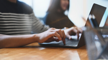 Close up view of young man hands typing on keyboard of laptop at modern co working office.