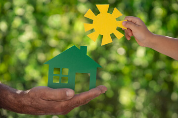 Wall Mural - Family holding eco house in hands against spring green background