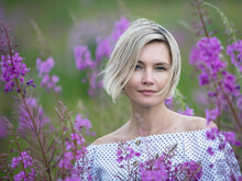 Portrait Of A Beautiful Middle-aged Woman Standing In A Blooming Field. Purple Flowers, Spring Landscape