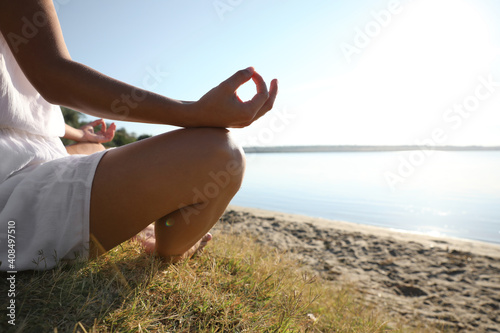 Young woman meditating near river at sunset, closeup view with space for text. Nature healing power