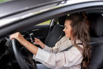 Poster - safety and people concept - happy smiling young woman or female driver with smartphone driving car in city