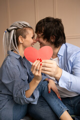 Young couple kissing with red heart valentine in hands. Celebrating Saint Valentine's Day.