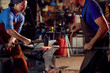Male And Female Blacksmiths Hammering Metalwork On Anvil With Sparks