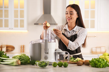 Poster - Young woman putting fresh kiwi and apple into juicer at table in kitchen