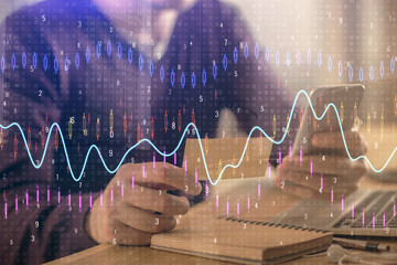 Double exposure of man's hands holding and using a phone and financial graph drawing. Analysis concept.