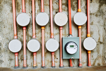 Abstract detail background view of a round electrical meter, surrounded by many unused round outlets and pvc pipes attached to a concrete wall