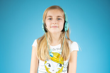 Cute adorable girl wearing headphones and enjoying music over blue background.